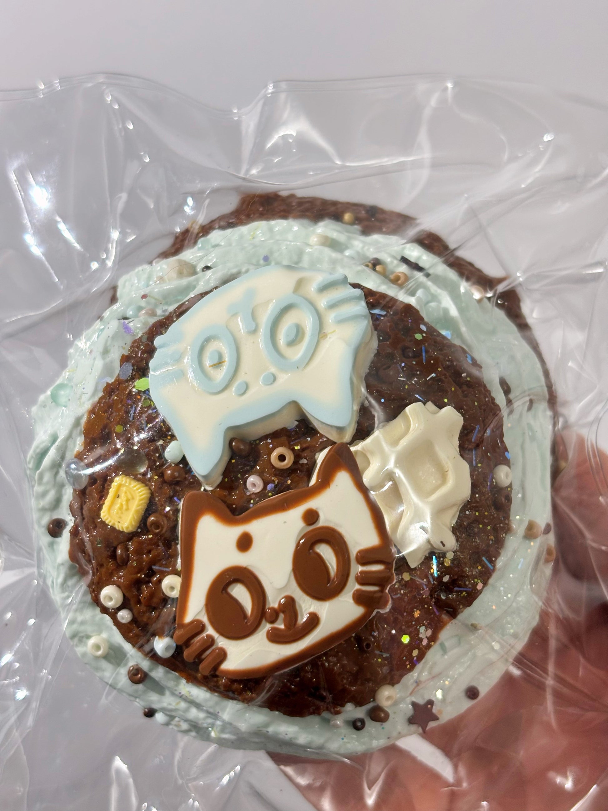 焼き菓子、丸型デコ。青緑の顔モチーフと白い飾り、チョコチップの粒