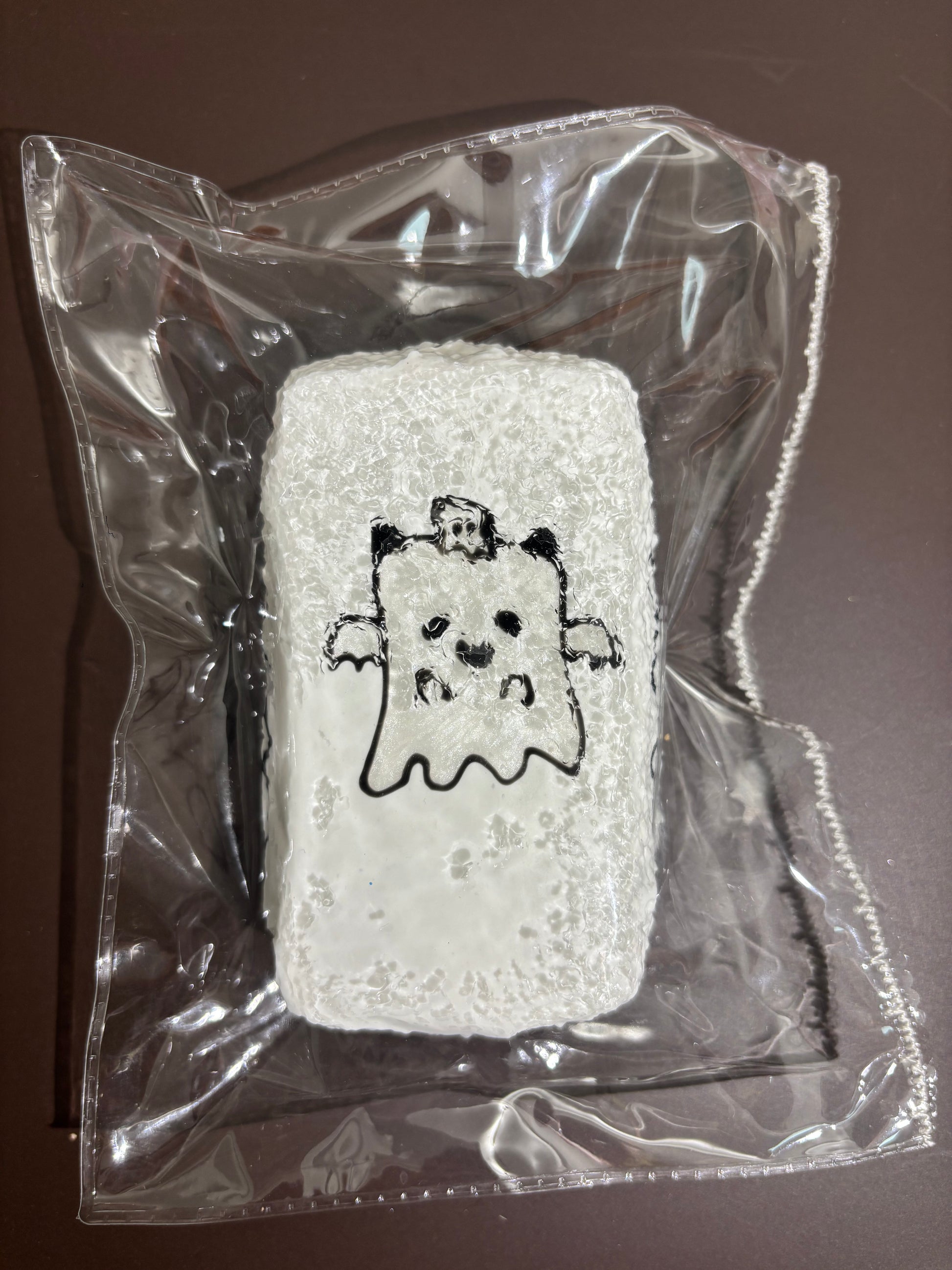 透明袋入りの白い刺繍布。手のあるクマ風キャラクターの刺繍。