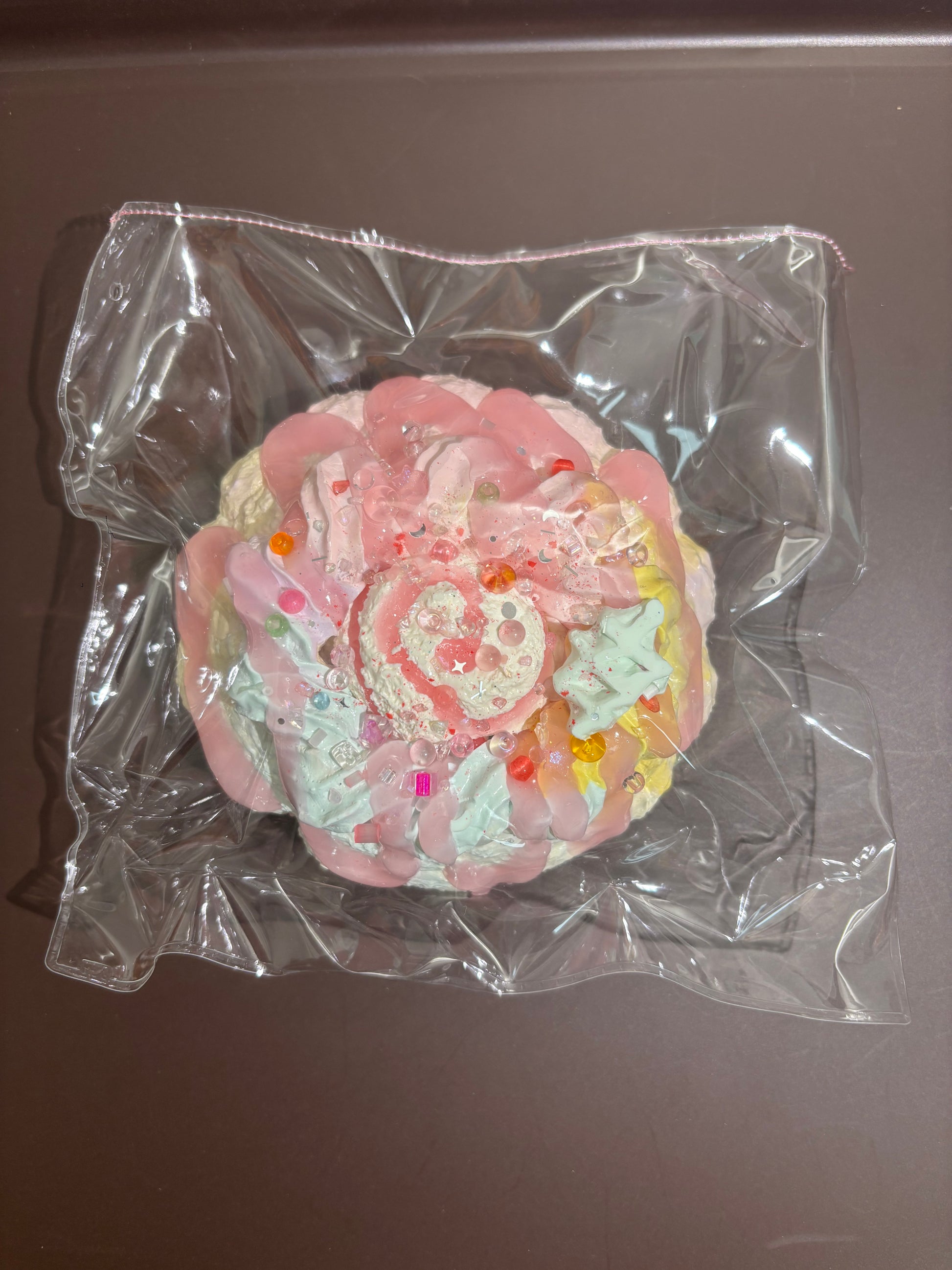 クリア袋入りの丸いデコレーション菓子、淡いピンクのクリームに飾り