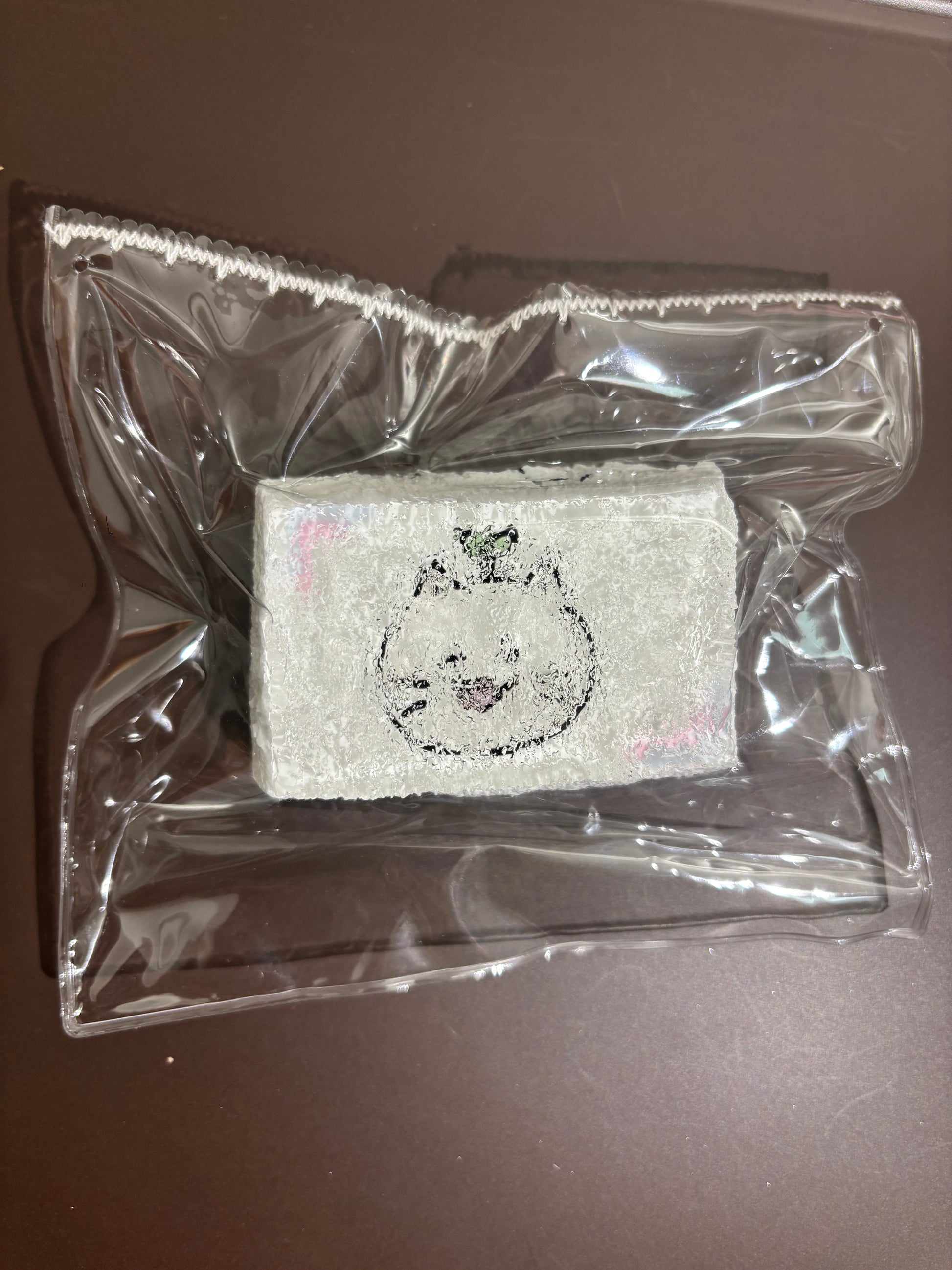 透明袋入りの白い刺繍布。丸いクマ風モチーフの刺繍が中央に入る。