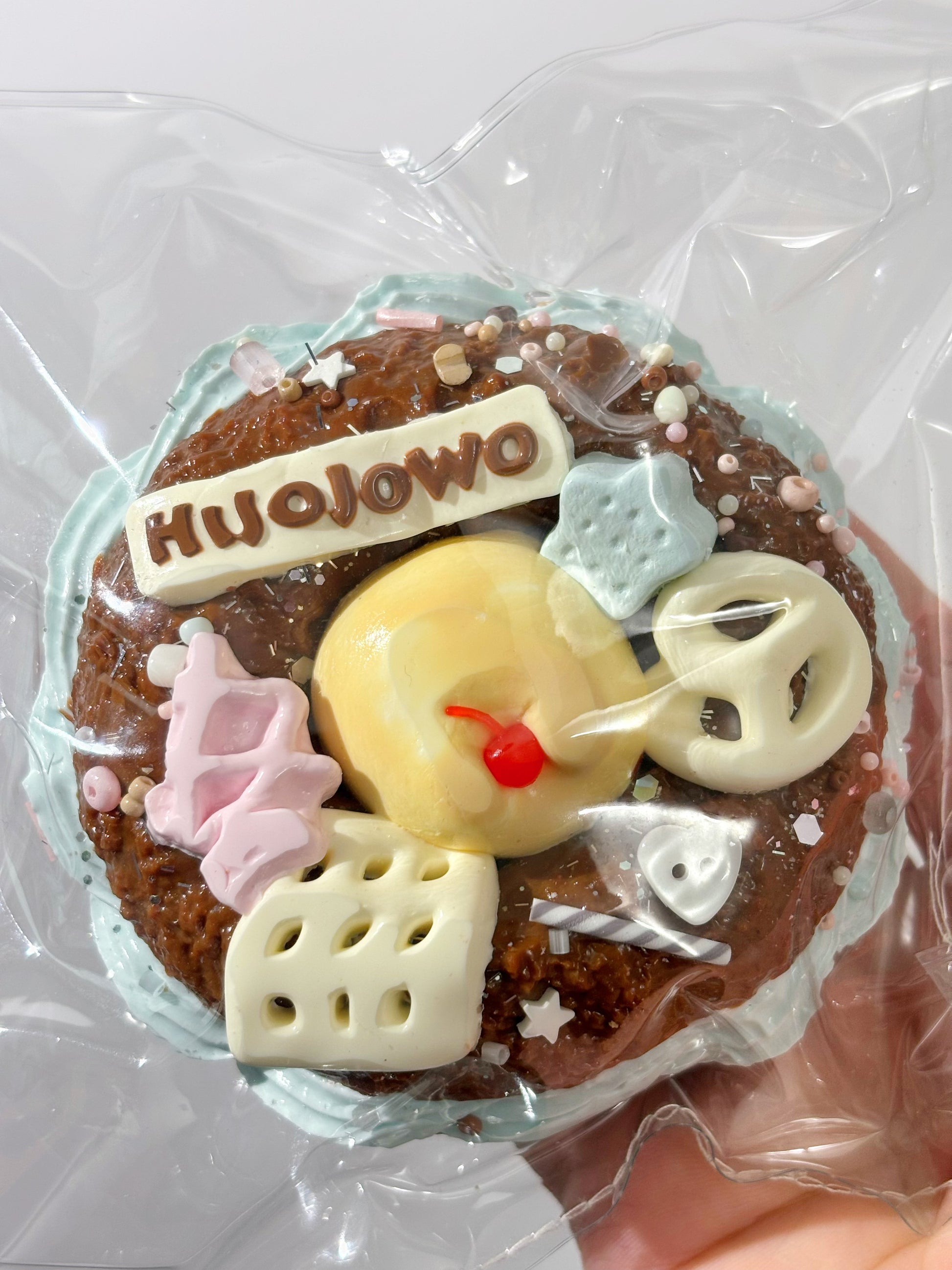 焼き菓子、丸型にデコ。HIJOJOWOロゴ付き、青緑の飾りと白いモチーフ