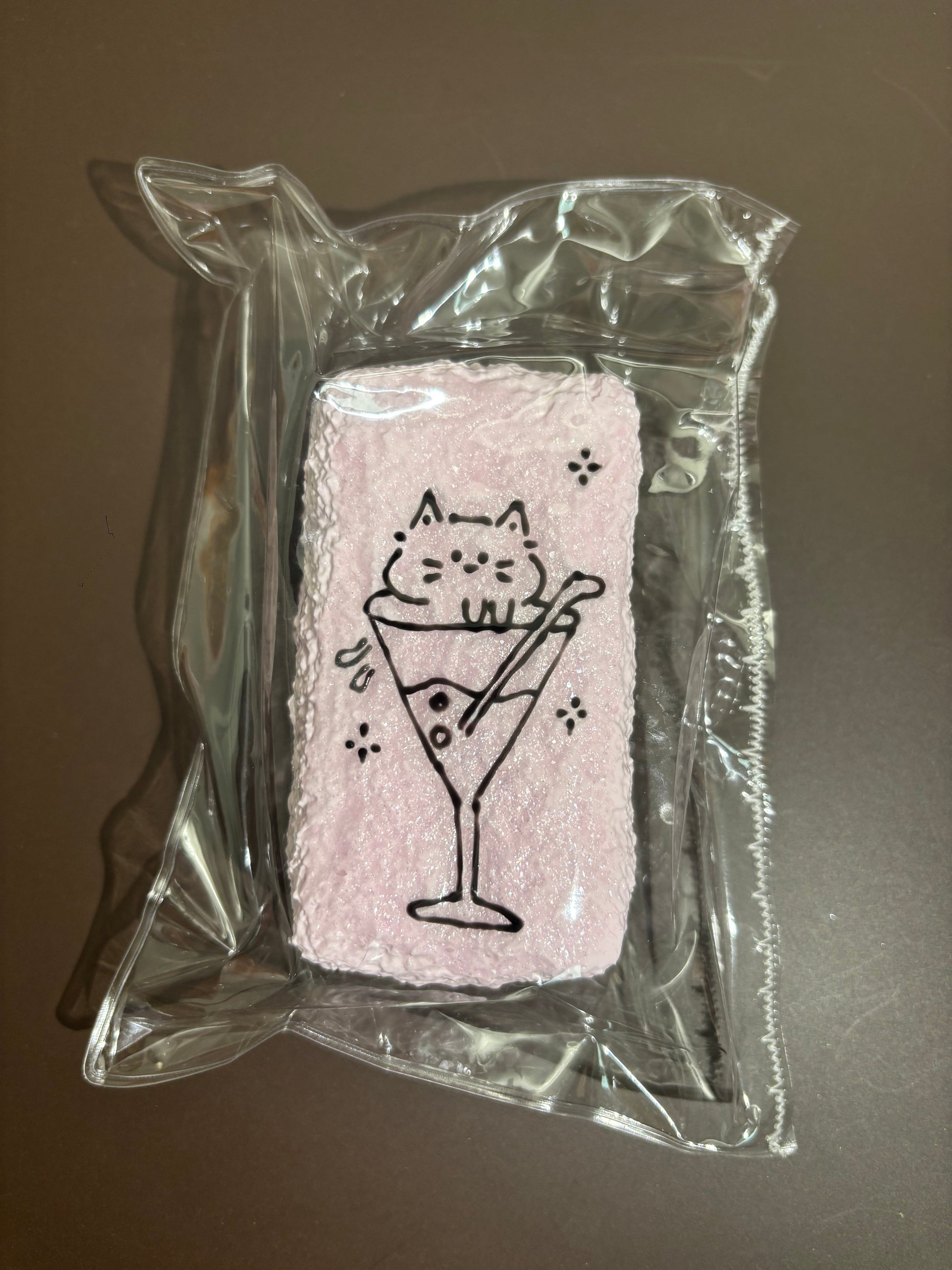 透明袋入りの白い刺繍布。グラスを持つネコ風のキャラクター刺繍。