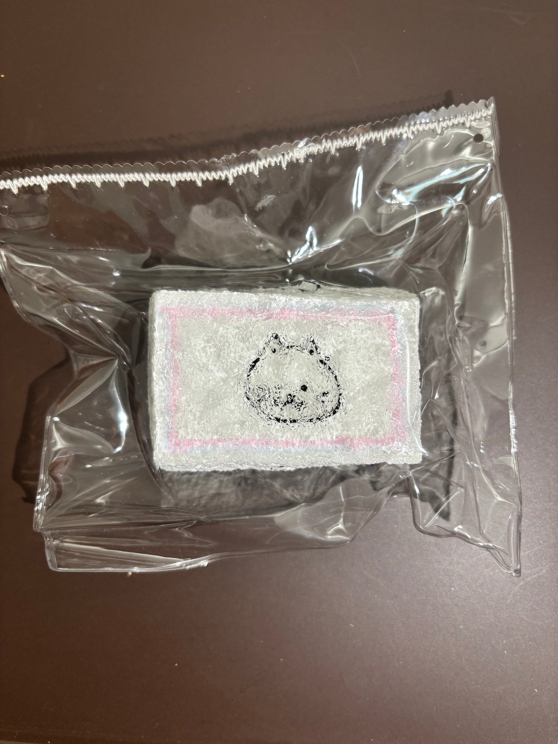 透明袋入りの白い刺繍布。中央の丸いクマ風顔刺繍、周囲は点々模様。