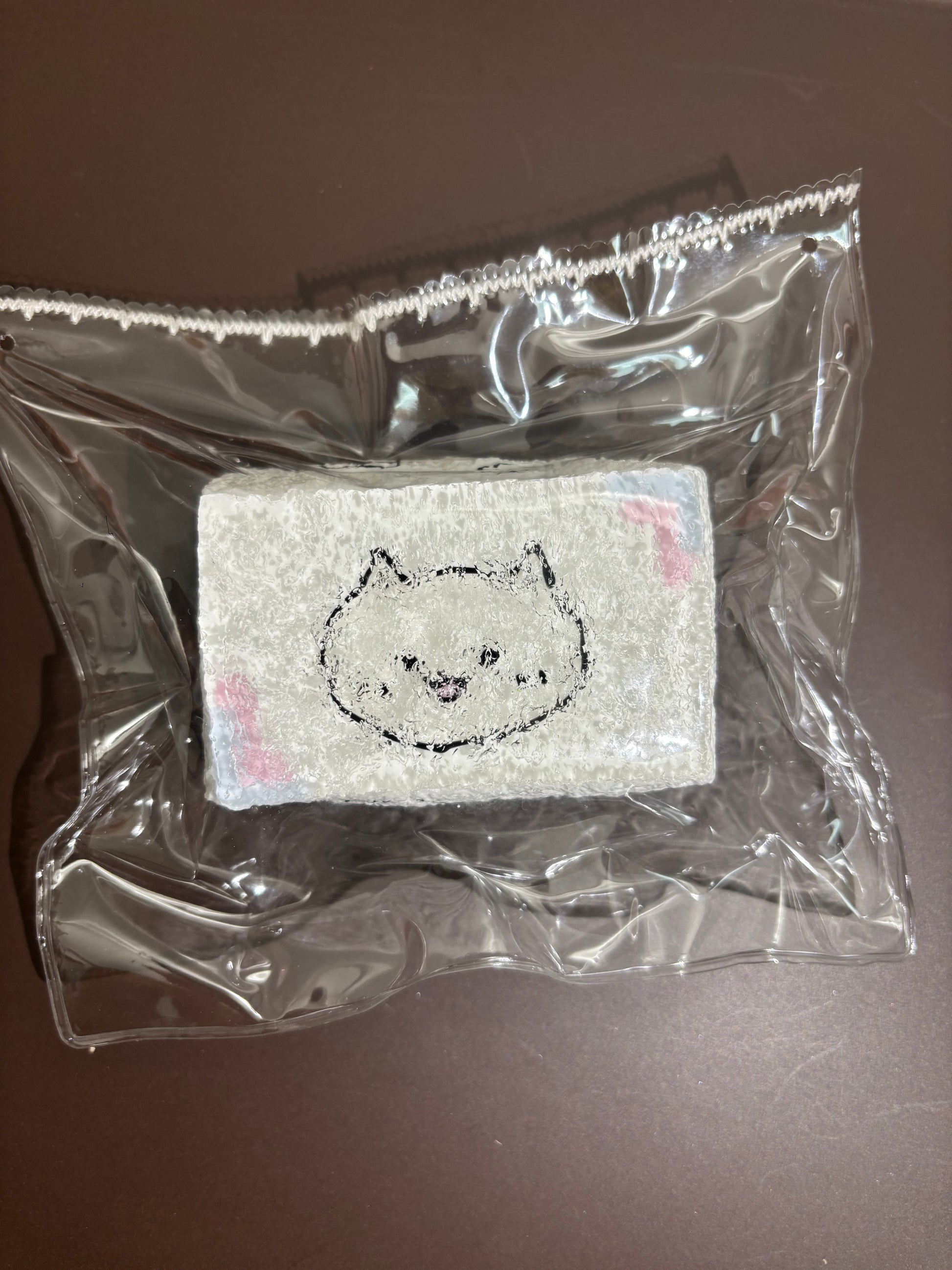 透明袋入りの白い刺繍布。クマ風顔の刺繍が正面に大きく配置。